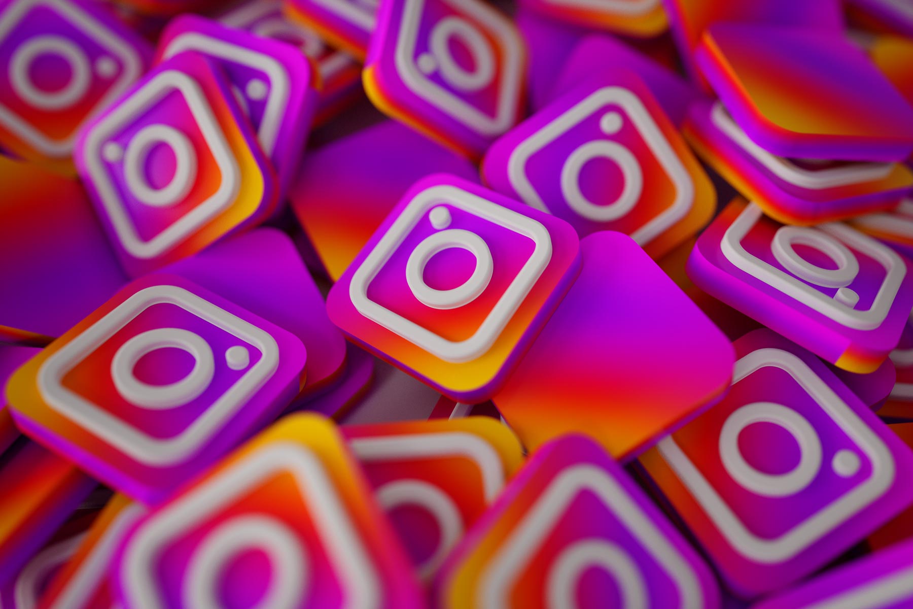 A pile of 3D Instagram logo icons in pink, purple and orange